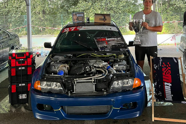 The BMW E46 with its bonnet open in the paddock, Tomasz holding the 1st-place trophy beside it