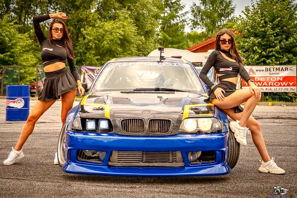 Two hostesses posing at the front of the BMW E46 during an event